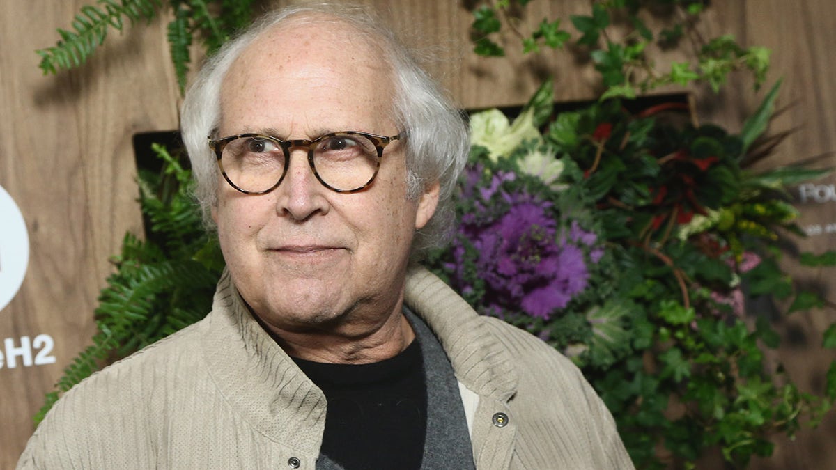 Chevy Chase wears khaki jacket over black T-shirt