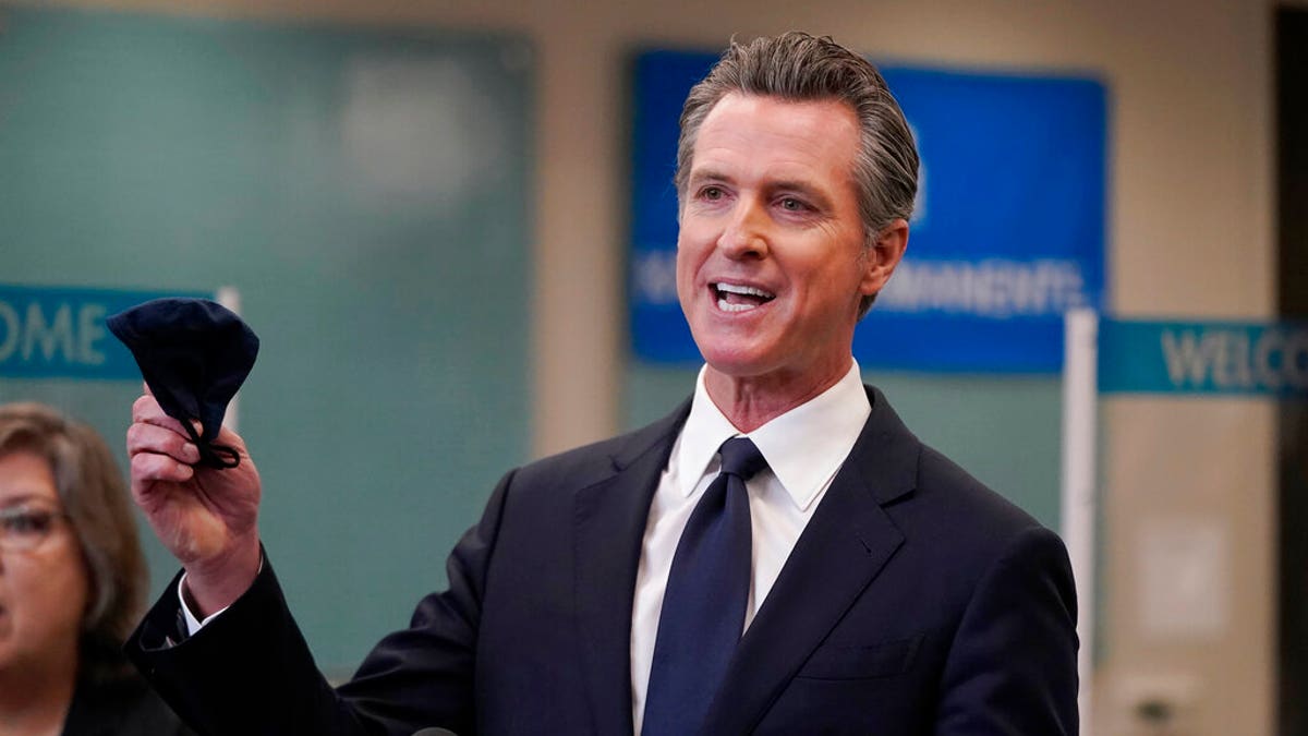 Gavin Newsom holds a mask at a California news conference