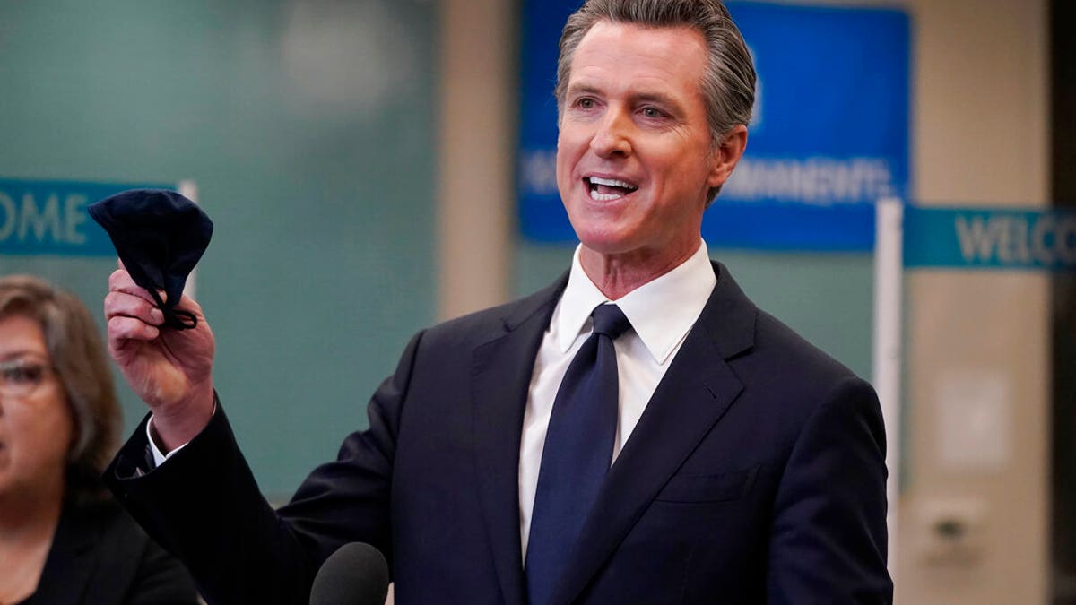 Gavin Newsom holds a mask at a California news conference