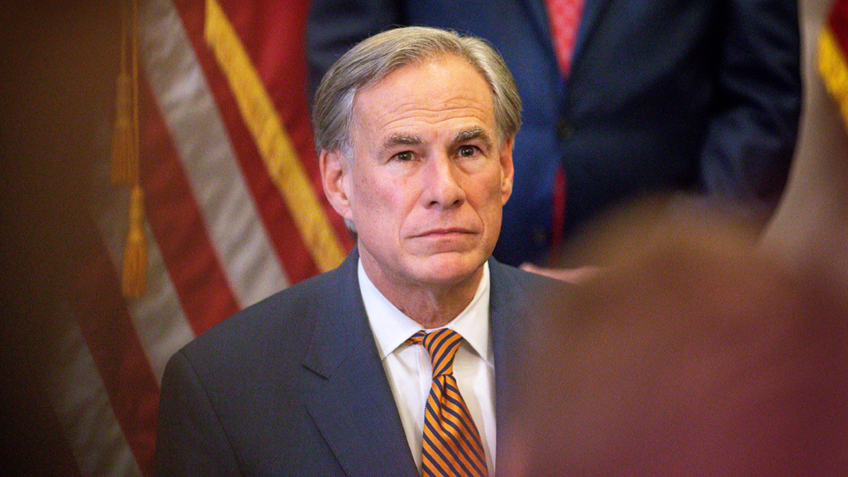 Greg Abbott in a gray suit and striped tie in front of an American flag