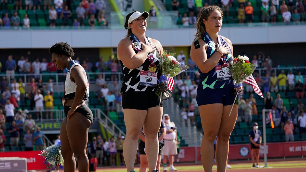 Gwendolyn Berry, left, looks away as DeAnna Price and Brooke Andersen stand for the national anthem after the finals of the women's hammer throw at the U.S. Olympic Track and Field Trials Saturday, June 26, 2021, in Eugene, Ore. Price won, Andersen was second and Berry finished third.