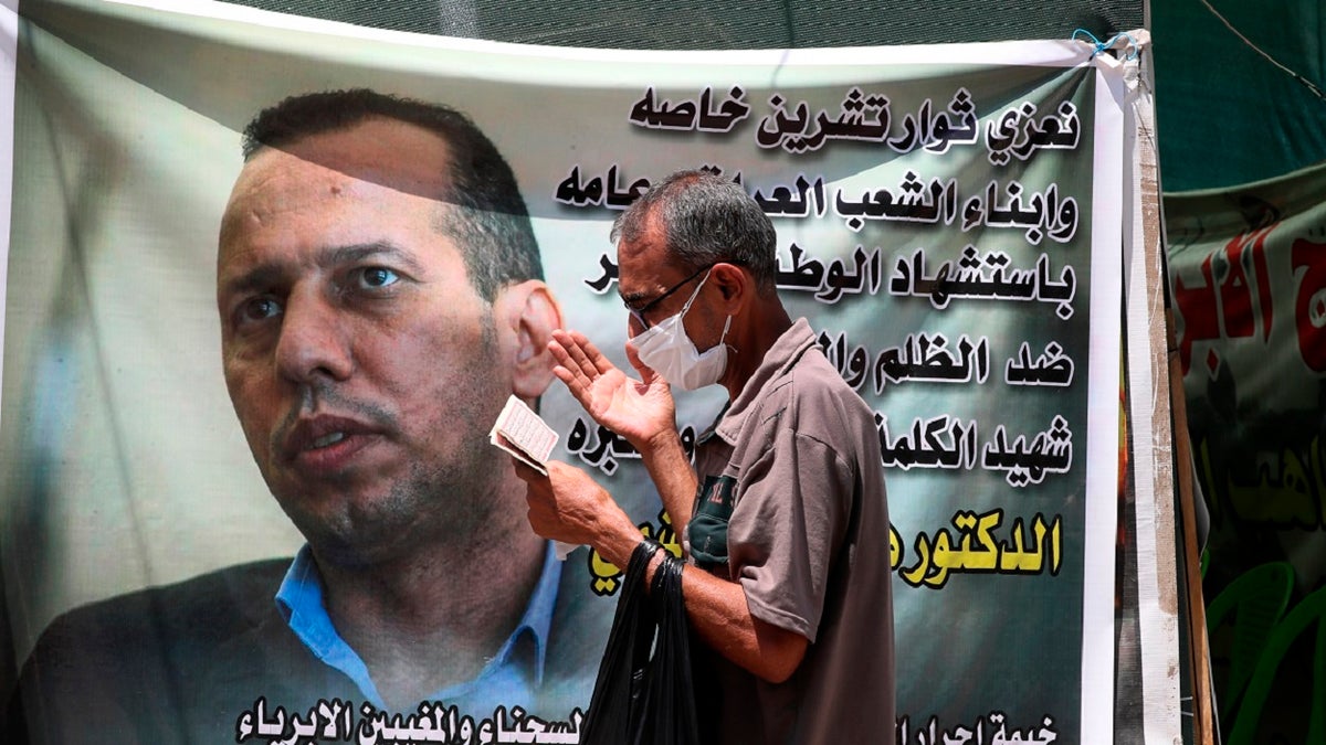 In this July 12, 2020 file photo, a protester prays by a poster showing Hisham al-Hashimi an Iraqi analyst who was a leading expert on the Islamic State and other armed groups who was shot dead in Baghdad. (AP Photo/Khalid Mohammed)