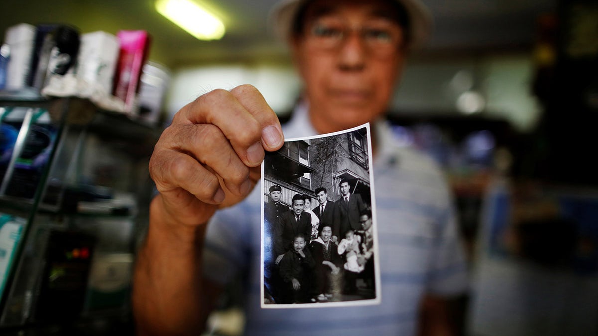 FILE PHOTO : Resident Kohei Jinno, 79, shows a photograph of himself (2nd L wearing suit) taken on January 2, 1957 in front of his previous home, at his shop inside Kasumigaoka apartment complex which is located near the National Olympic Stadium in Tokyo September 18, 2013.