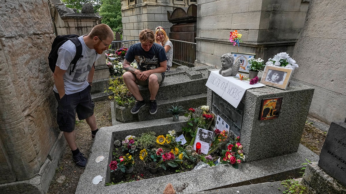 Joachim Tittmar from Germany, left, Walter Homburg of the Netherlands, center, and his girlfriend Kate Schirm gather at the tomb of rock singer Jim Morrison at the Pere-Lachaise cemetery in Paris, Saturday, July 3, 2021. (Associated Press)