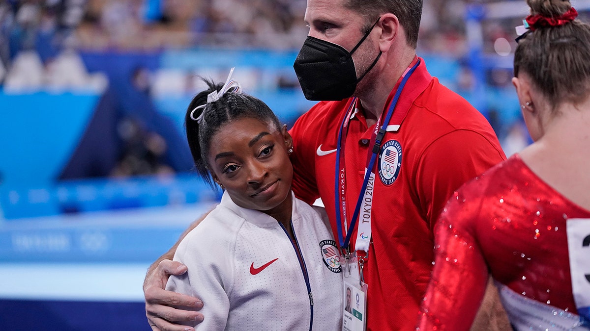 Coach Laurent Landi embraces Simone Biles after she exited the team final with apparent injury at the 2020 Summer Olympics, Tuesday, July 27, 2021, in Tokyo. The 24-year-old reigning Olympic gymnastics champion Biles huddled with a trainer after landing her vault. She then exited the competition floor with the team doctor. (AP Photo/Gregory Bull)