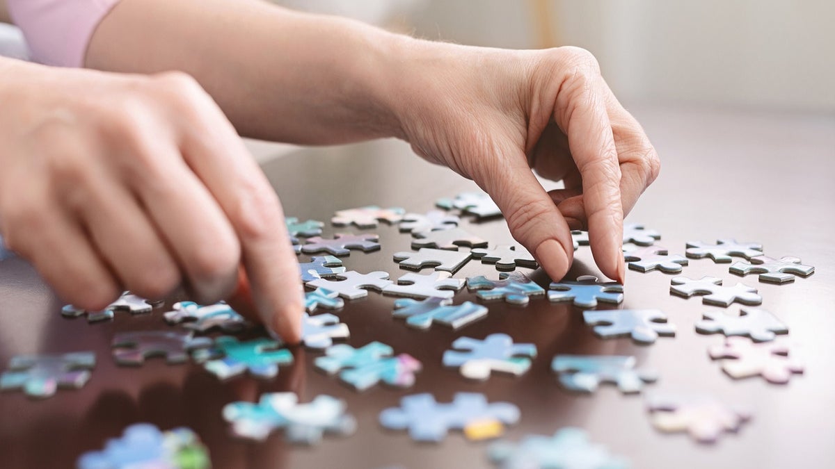 Dementia prevention. Elderly woman hands doing jigsaw puzzle at home, panorama, close up