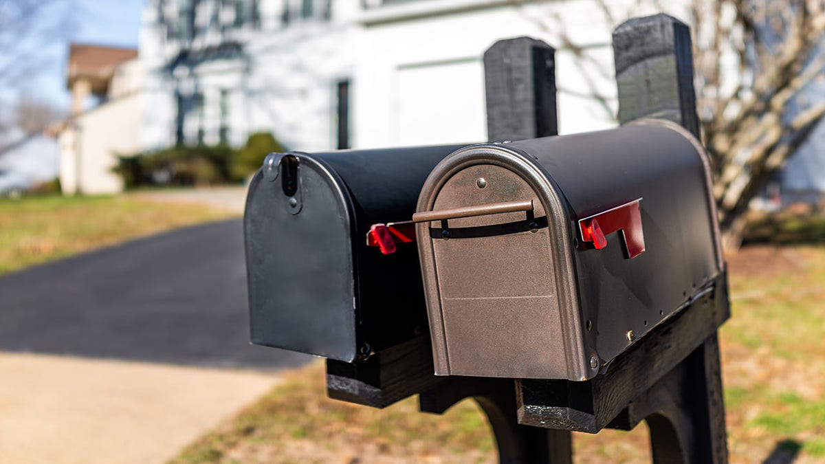 Close-up of two modern black and brown metal red flag mailboxes on a single family home in a residential suburb with no one and a house in the background
