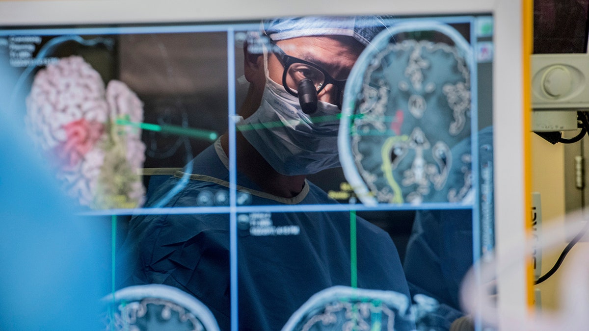 In this 2017 photo provided by the University of California, San Francisco, neurosurgeon Dr. Edward Chang is reflected in a computer monitor displaying brain scans as he performs surgery at UCSF. 
