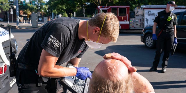 A paramedic with Falck Northwest ambulances treats a man experiencing heat exposure during a heat wave, Saturday, June 26, 2021, in Salem, Ore. (AP Photo/Nathan Howard)