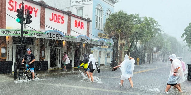 Determined visitors head for Sloppy Joe's Bar while crossing a flooded Duval Street as heavy winds and rain pass over Key West, フラ。, 火曜日, 7月 6, 2021. (Rob O'Neal/The Key West Citizen via AP)