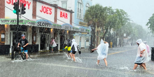 Determined visitors head for Sloppy Joe's Bar while crossing a flooded Duval Street as heavy winds and rain pass over Key West, Fla., Tuesday, July 6, 2021. (Rob O'Neal/The Key West Citizen via AP)