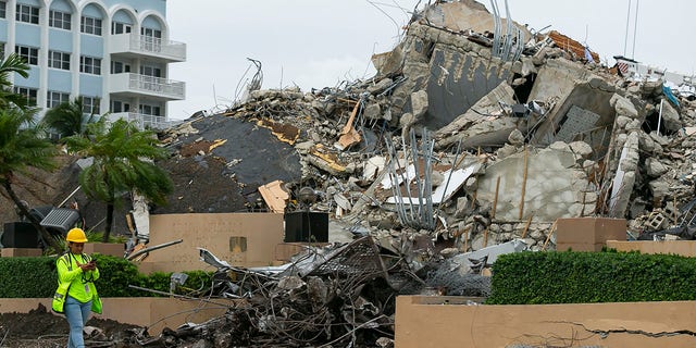 A workers make her way past the rubble and debris of the Champlain Towers South condo in Surfside, 弗拉. 星期二, 七月 6, 2021.  Officials overseeing the search at the site of the Florida condominium collapse seem increasingly somber about the prospects for finding anyone alive.  (Matias J. Ocner/Miami Herald via AP)