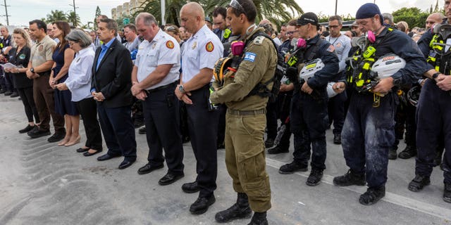 Miami-Dade County officials, members of search and rescue teams and Miami-Dade Fire Rescue, along with police and workers who have been working at the site of the collapse, gather for a moment of prayer and silence in front of the rubble at the site of the Champlain Towers South condominium collapse, Wednesday, July 7, 2021, in Surfside, Fla. (Jose A Iglesias/Miami Herald via AP)