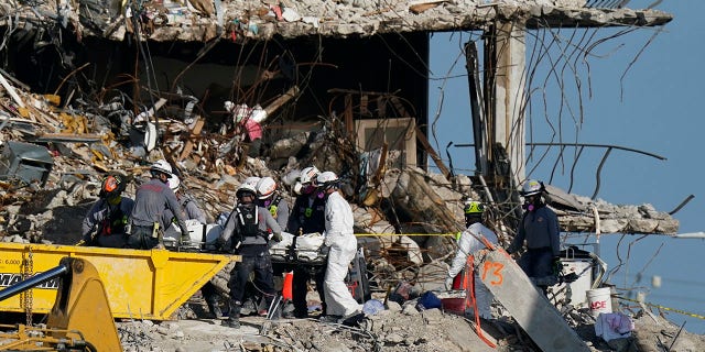 Search and rescue personnel remove remains on a stretcher as they work atop the rubble at the Champlain Towers South condominium building.