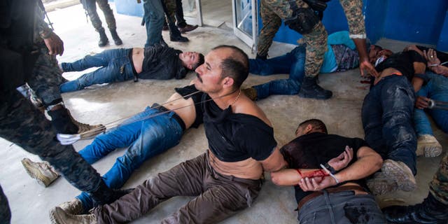 Suspects in the assassination of Haiti's President Jovenel Moise sit on the floor after being detained, at the General Direction of the police in Port-au-Prince, Haiti, Thursday, July 8, 2021. A Haitian judge involved in the murder investigation said that President Moise was shot a dozen times and that his office and bedroom were ransacked. (AP Photo/Jean Marc Hervé Abélard)