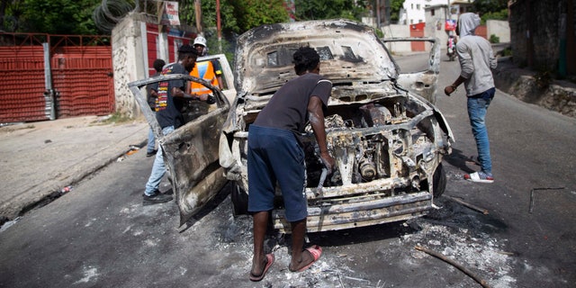 People try to recover usable material from a burned-out car during a protest a day after the murder of President Jovenel Moise, in Port-au-Prince, Haiti, Thursday, July 8, 2021. Moise was assassinated after a group of armed men attacked his private residence, and gravely wounding his wife, First Lady Martine Moise. (AP Photo/Joseph Odelyn)