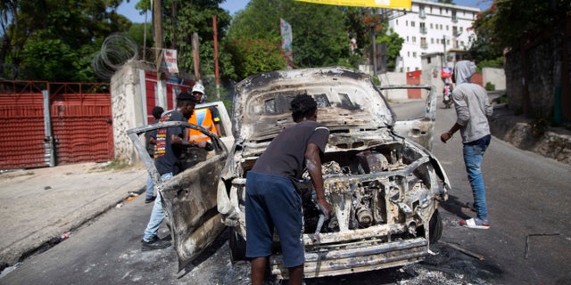 People attempt to retrieve usable equipment from a burnt out car during a protest a day after the murder of President Jovenel Moise, in Port-au-Prince, Haiti, on Thursday, July 8, 2021. Moise was assassinated after a group of gunmen attacked his private residence and seriously injured his wife, First Lady Martine Moise. (AP Photo / Joseph Odelyn)