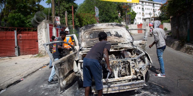 People try to recover usable material from a burned-out car during a protest a day after the murder of President Jovenel Moise, in Port-au-Prince, Haiti, Thursday, July 8, 2021. Moise was assassinated after a group of armed men attacked his private residence, and gravely wounding his wife, First Lady Martine Moise. (AP Photo/Joseph Odelyn)