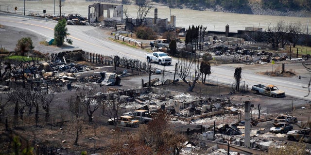 A Royal Canadian Mounted Police (RCMP) vehicle drives past the remains of vehicles and structures in Lytton, British Columbia, Friday, July 9, 2021, after a wildfire destroyed most of the village on June 30. (Darryl Dyck/The Canadian Press via AP)