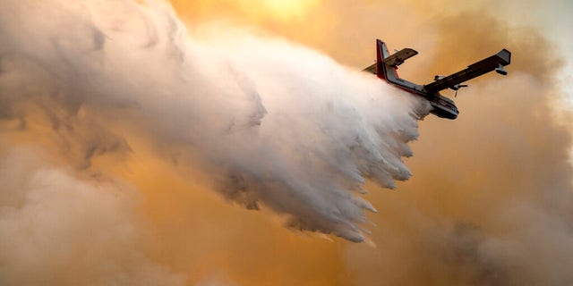 A scoop plane drops water onto a burning ridge where a fire line had been created by crews of wildland firefighters, Monday, July 12, 2021, at the Lick Creek Fire, south of Asotin, Wash. (Pete Caster/Lewiston Tribune via AP)