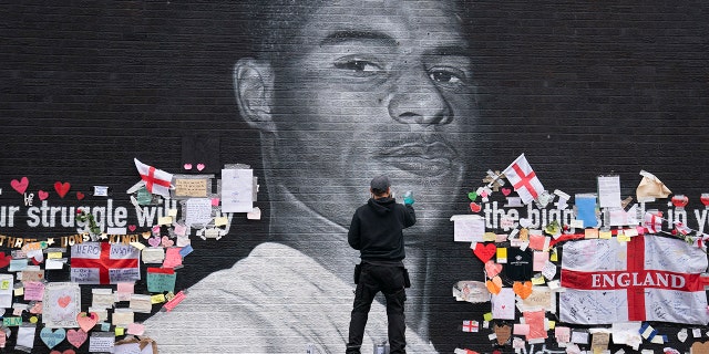 Street artist Akse P19 repairs the mural of Manchester United striker Marcus Rashford in Manchester on July 13, 2021. The mural was defaced after England lost the Euro 2020 soccer championship to Italy. (AP Photo/Jon Super)