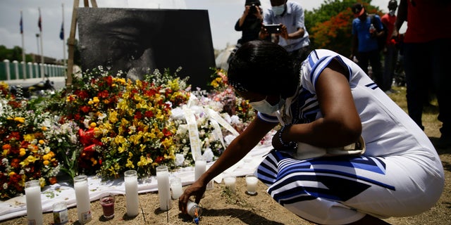 A woman lights a candle at a memorial outside the Presidential Palace in memory of slain President Jovenel Moise in Port-au-Prince, Haiti, Wednesday, July 14, 2021, a week after Moise was assassinated in his home. (AP Photo/Joseph Odelyn)