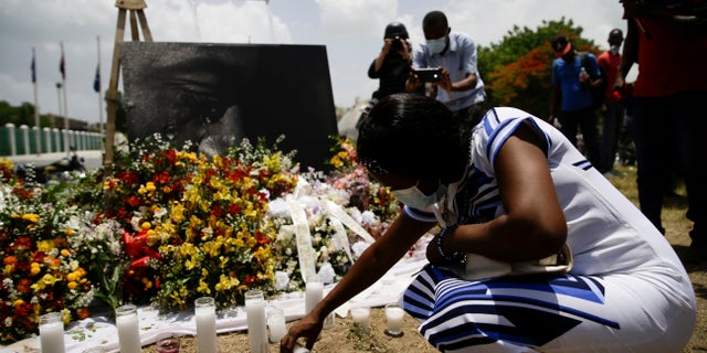 A woman lights a candle at a memorial outside the Presidential Palace in memory of slain President Jovenel Moise in Port-au-Prince, Haiti, Wednesday, July 14, 2021, a week after Moise was assassinated in his home. (AP Photo/Joseph Odelyn)