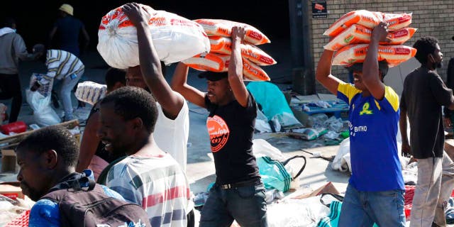 People carry bags of rice from a factory in Mobeni, south of Durban South Africa, Thursday, July 15, 2021, as unrest continues in the KwaZulu Natal province. 