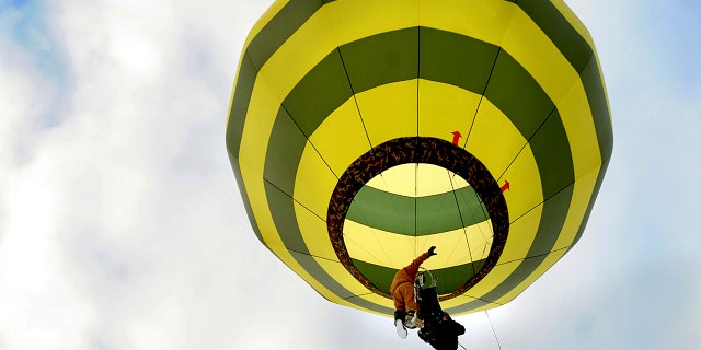 In a harness he created, Brian Boland, of Post Mills, Vermont, takes off attached to a hot-air balloon with a passenger above Westshire Elementary School in West Fairlee, Vt., on Feb. 26, 2013. (Associated Press)