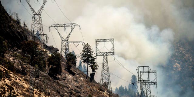 Smoke billows behind power lines as the Dixie Fire burns along Highway 70 in Plumas National Forest, Calif., on Friday, July 16, 2021.