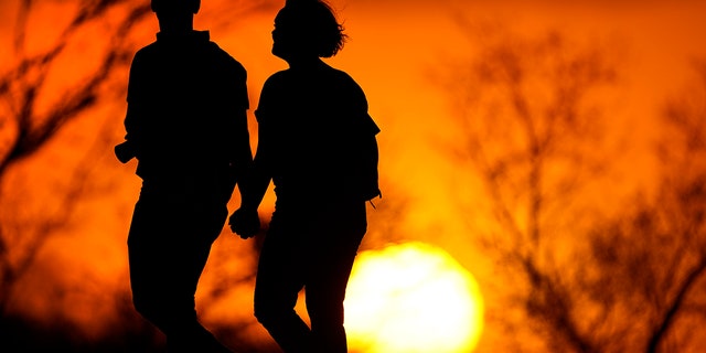 A couple stroll through a park at sunset in Kansas City, Mo on March 10, 2021 (AP Photo / Charlie Riedel, File)