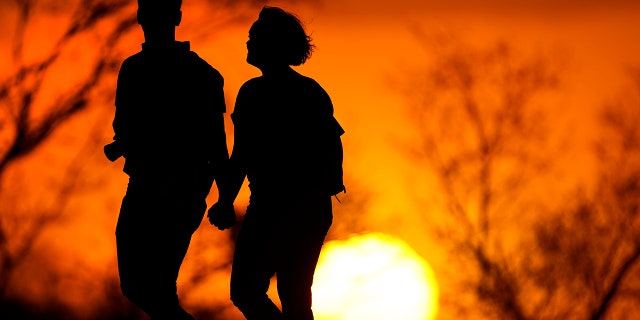 A couple walks through a park at sunset in Kansas City, Mo on March 10, 2021. (AP Photo/Charlie Riedel, File)