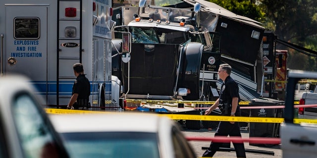 In this July 1, 2021 file photo Police officers walk past the remains of an armored Los Angeles Police Department tractor-trailer, after illegal fireworks seized at a South Los Angeles home exploded, in South Los Angeles. (AP Photo/Damian Dovarganes,File)