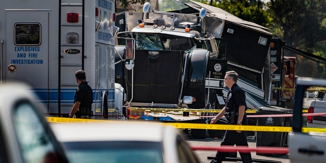 In this July 1, 2021 file photo Police officers walk past the remains of an armored Los Angeles Police Department tractor-trailer, after illegal fireworks seized at a South Los Angeles home exploded, in South Los Angeles. (AP Photo/Damian Dovarganes,File)