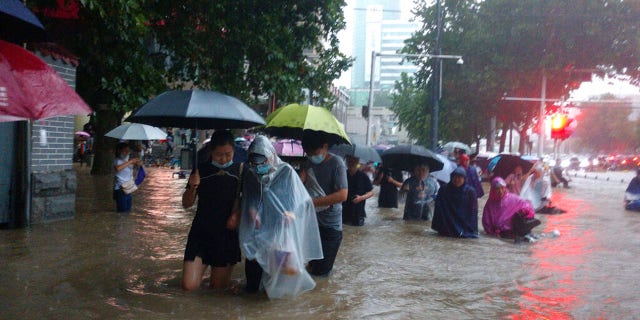 People move through flood water after a heavy downpour in Zhengzhou city, central China's Henan province on Tuesday, July 20, 2021. Heavy flooding has hit central China following unusually heavy rains, with the subway system in the city of Zhengzhou inundated with rushing water and thousands of residents having to be relocated. (Chinatopix Via AP)