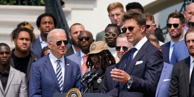 President Joe Biden, surrounded by members of the Tampa Bay Buccaneers, listens as Tampa Bay Buccaneers quarterback Tom Brady speaks during a ceremony on the South Lawn of the White House, in Washington, Tuesday, July 20, 2021. (AP Photo/Manuel Balce Ceneta)