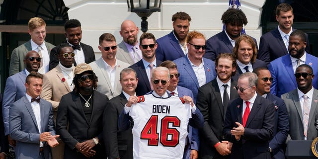 President Joe Biden, surrounded by members of the Tampa Bay Buccaneers, poses for a photo holding a jersey during a ceremony on the South Lawn of the White House in Washington on Tuesday, July 20, 2021 (AP Photo / Andrew Harnik)