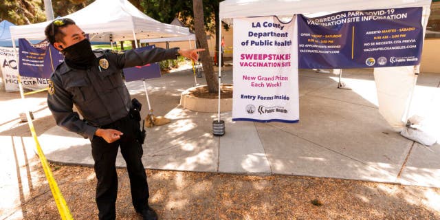 A private security guard gives directions to people looking to get vaccinated, as banners advertise the availability of the Johnson & Johnson and Pfizer COVID-19 vaccines at a county-run vaccination site offering free walk-in with no appointment needed in Los Angeles.