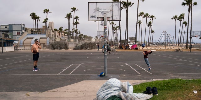 People play basketball as a homeless man sleeps near the court in the Venice neighborhood of Los Angeles, Tuesday, June 29, 2021. 