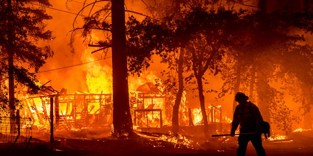 A firefighter passes a burning home as the Dixie Fire flares in Plumas County, Calif., Saturday, July 24, 2021. The fire destroyed multiple residences as it tore through the Indian Falls community. (AP Photo/Noah Berger)