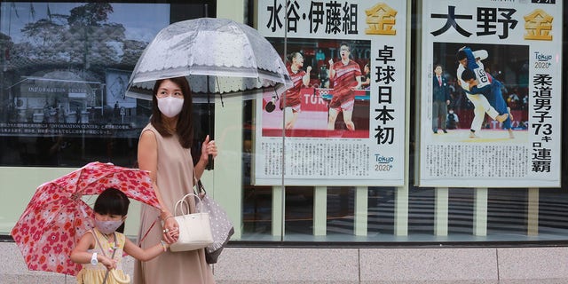 People wearing face masks to protect against the spread of the coronavirus walk past extra papers reporting on Japanese gold medalists at Tokyo Olympics, in Tokyo Tuesday, 7月 27, 2021. (AP Photo/Koji Sasahara)