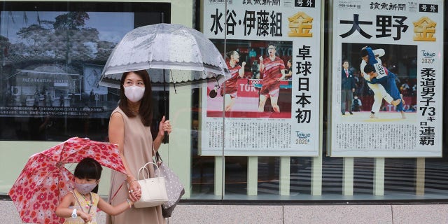 People wearing face masks to protect against the spread of the coronavirus walk past extra papers reporting on Japanese gold medalists at Tokyo Olympics, in Tokyo Tuesday, July 27, 2021. (AP Photo/Koji Sasahara)