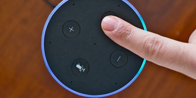 A finger pressing a button on an Amazon Echo device