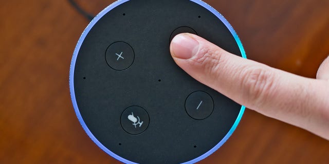 A finger pressing a button on an Amazon Echo device