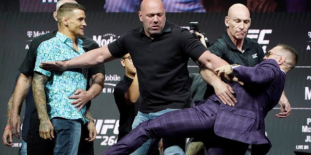 Conor McGregor, right, kicks at Dustin Poirier, left, as Dana White, UFC President, holds them apart during a news conference for a UFC 264 mixed martial arts bout Thursday, July 8, 2021, in Las Vegas. (AP Photo/John Locher)