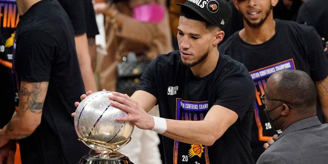 Phoenix Suns guard Devin Booker rubs the Western Conference trophy after they won Game 6 of the NBA basketball Western Conference Finals against the Los Angeles Clippers Wednesday, June 30, 2021, in Los Angeles. The Suns won the game 130-103 to take the series 4-2. (AP Photo/Mark J. Terrill)