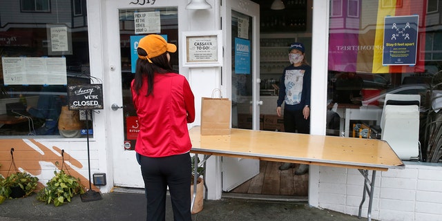 Cassava restaurant co-owner Yuka Ioroi, right, greets a customer picking up a to-go order in San Francisco, April 8, 2020. The restaurant plans to reopen indoor dining in August. (Getty Images)