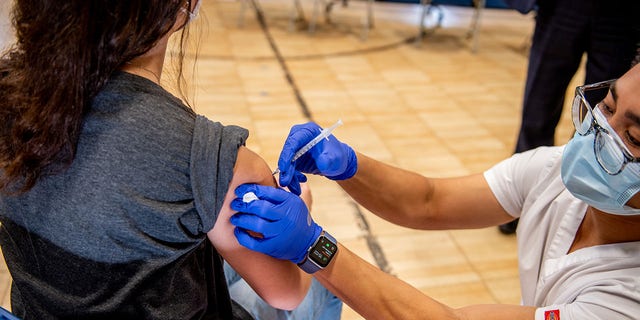 A healthcare worker administers a Covid-19 vaccine to a teenager in New York.  A California law that would allow teens to be vaccinated without parental consent is being changed, increasing the minimum age to 15 instead.