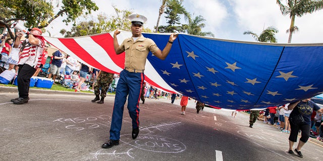 A U.S. Marine and parade goers carry a large American flag during the Coronado Fourth of July Parade on July 3, 2021 in Coronado, California.