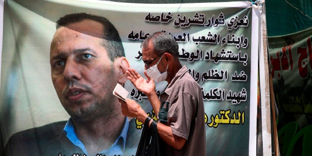 In this July 12, 2020 file photo, a protester prays by a poster showing Hisham al-Hashimi an Iraqi analyst who was a leading expert on the Islamic State and other armed groups who was shot dead in Baghdad. (AP Photo/Khalid Mohammed)